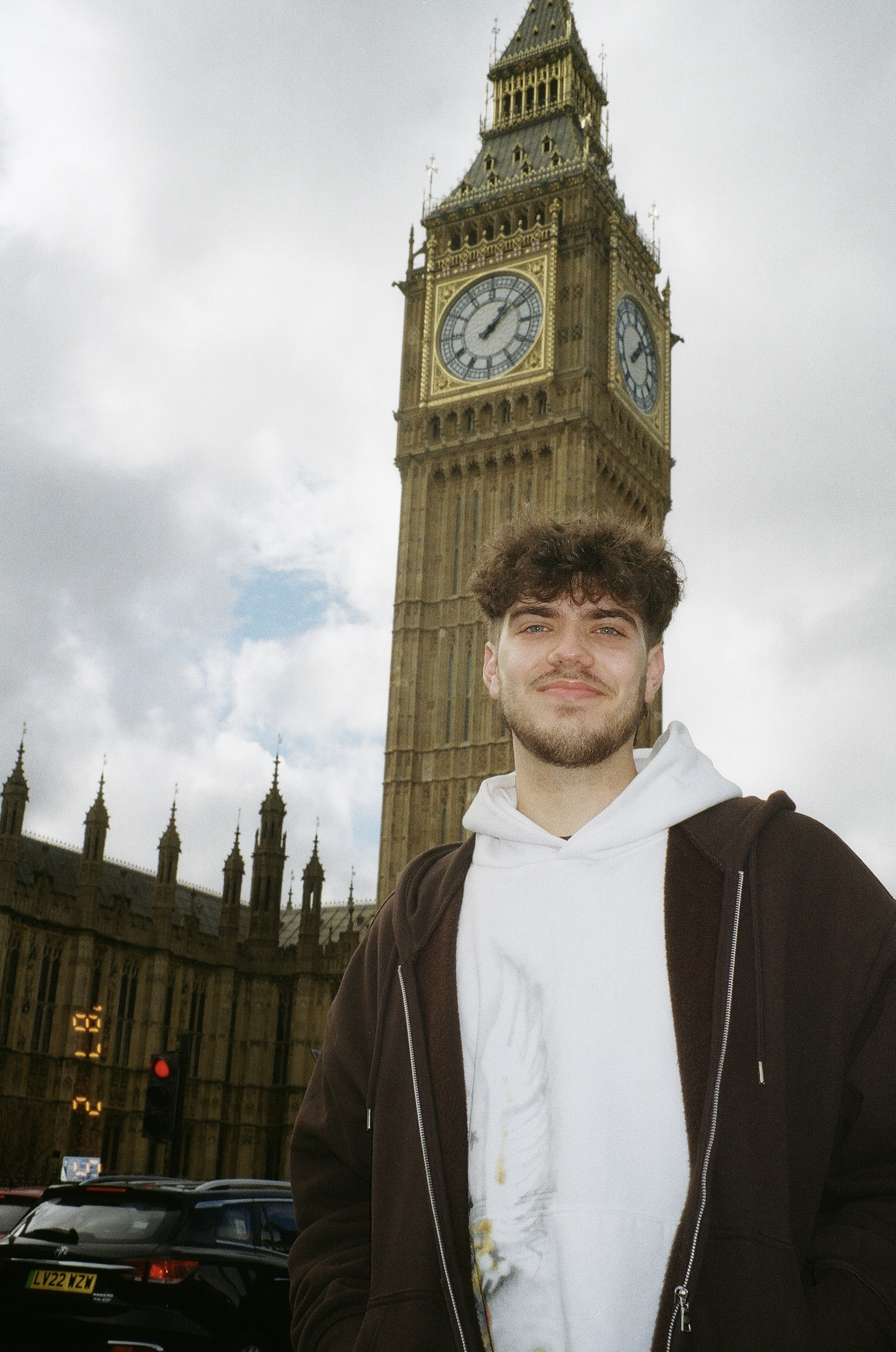 This photo depicts an image of a 20 year old boy with brown hair and a brown hoodie standing in front of the Big Ben in London, England.
