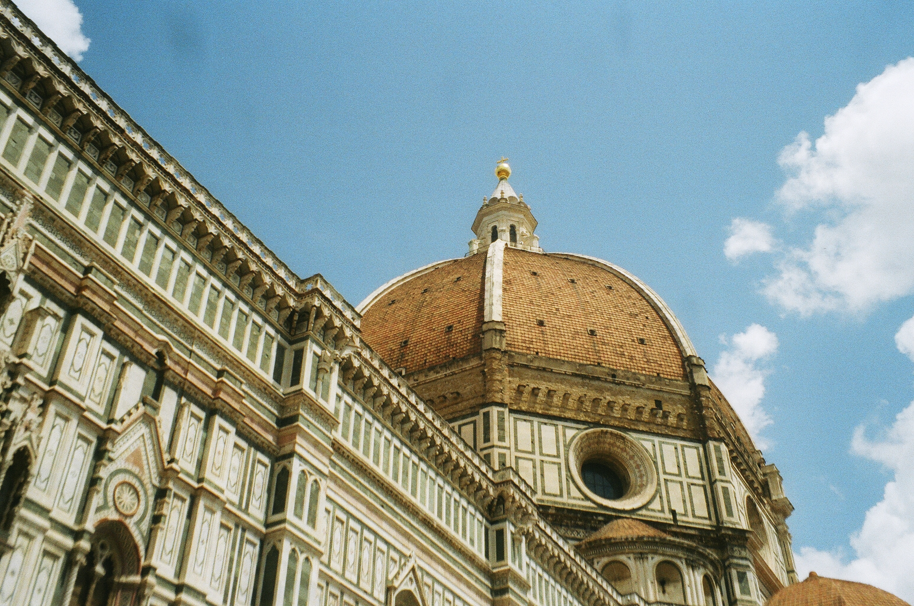 This image depicts a beuatiful angle of the world famous Duomo in Florence Italy. You can see the clay red tiles of the roof of the dome and the beautiful architecture with the stones building up to it.