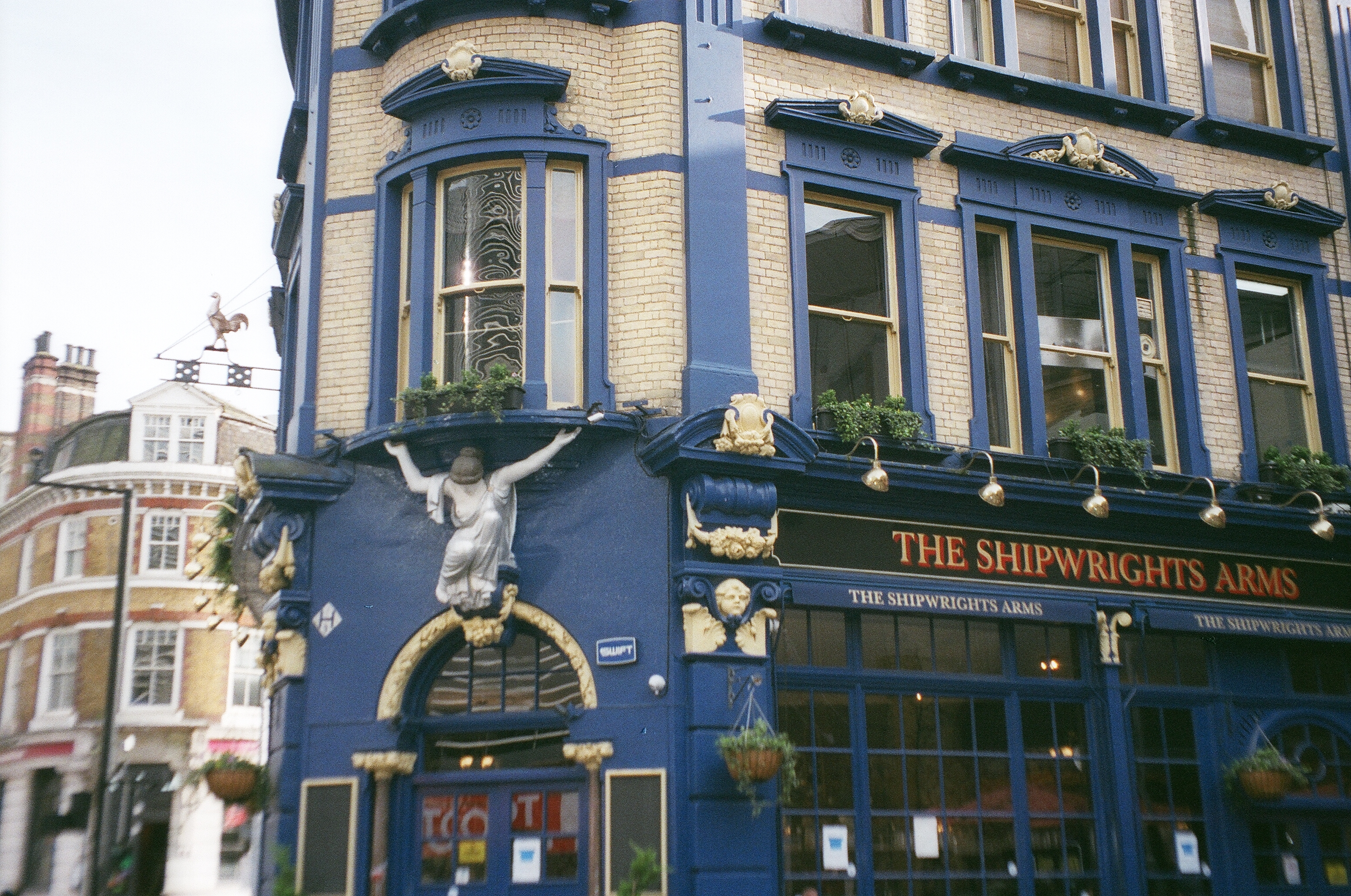 This image depicts a quaint pub in London, England, seemingly on a corner. The pub is a nice blue color and is called The Shipwrights Arms.