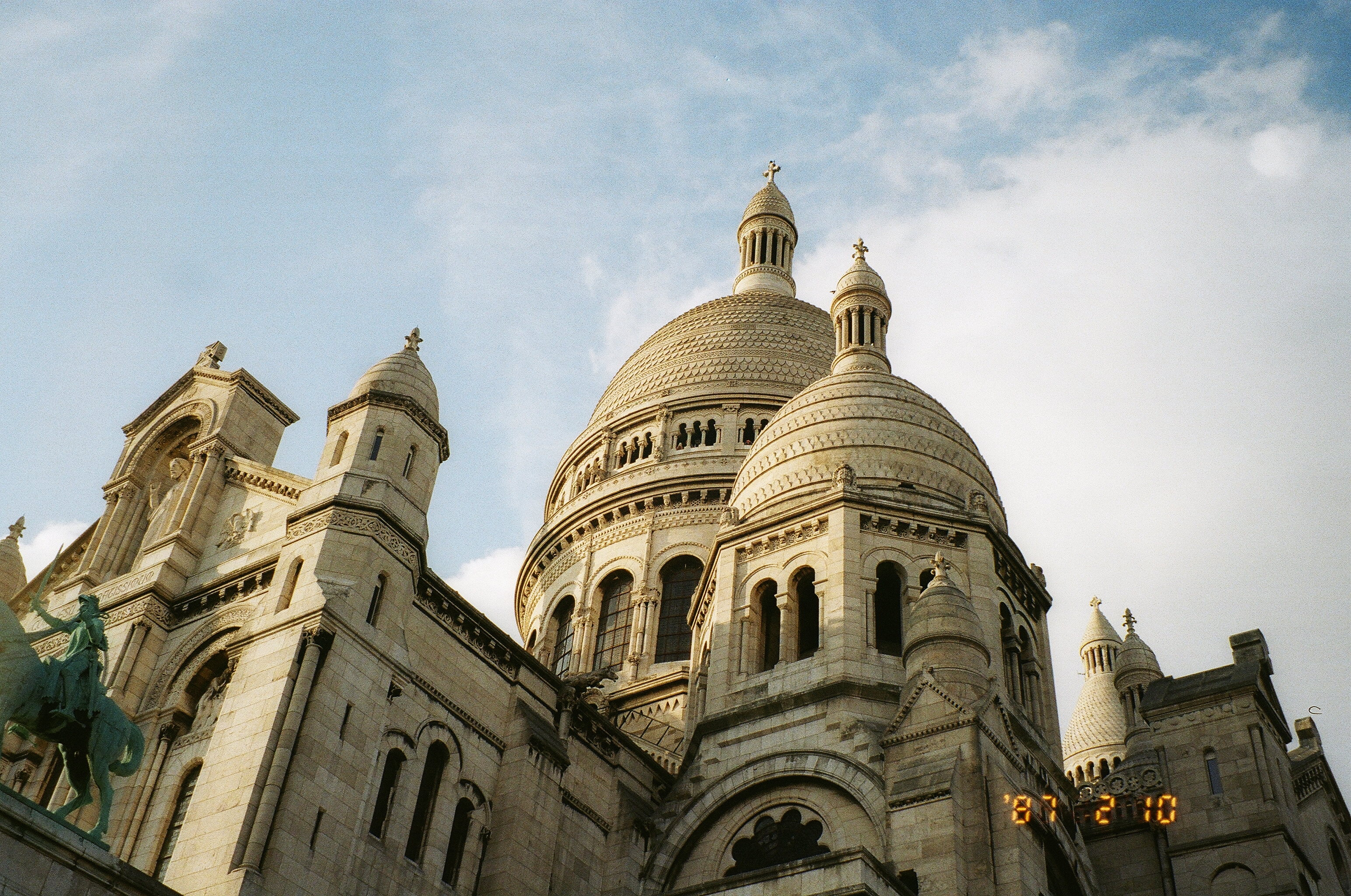 This image depicts an up angle shot of the Sacre Coeur Cathedral in Montmarte Paris, France. The Cathedral is made up of a series of Domes with an all white facade and gorgeous windows built in. 