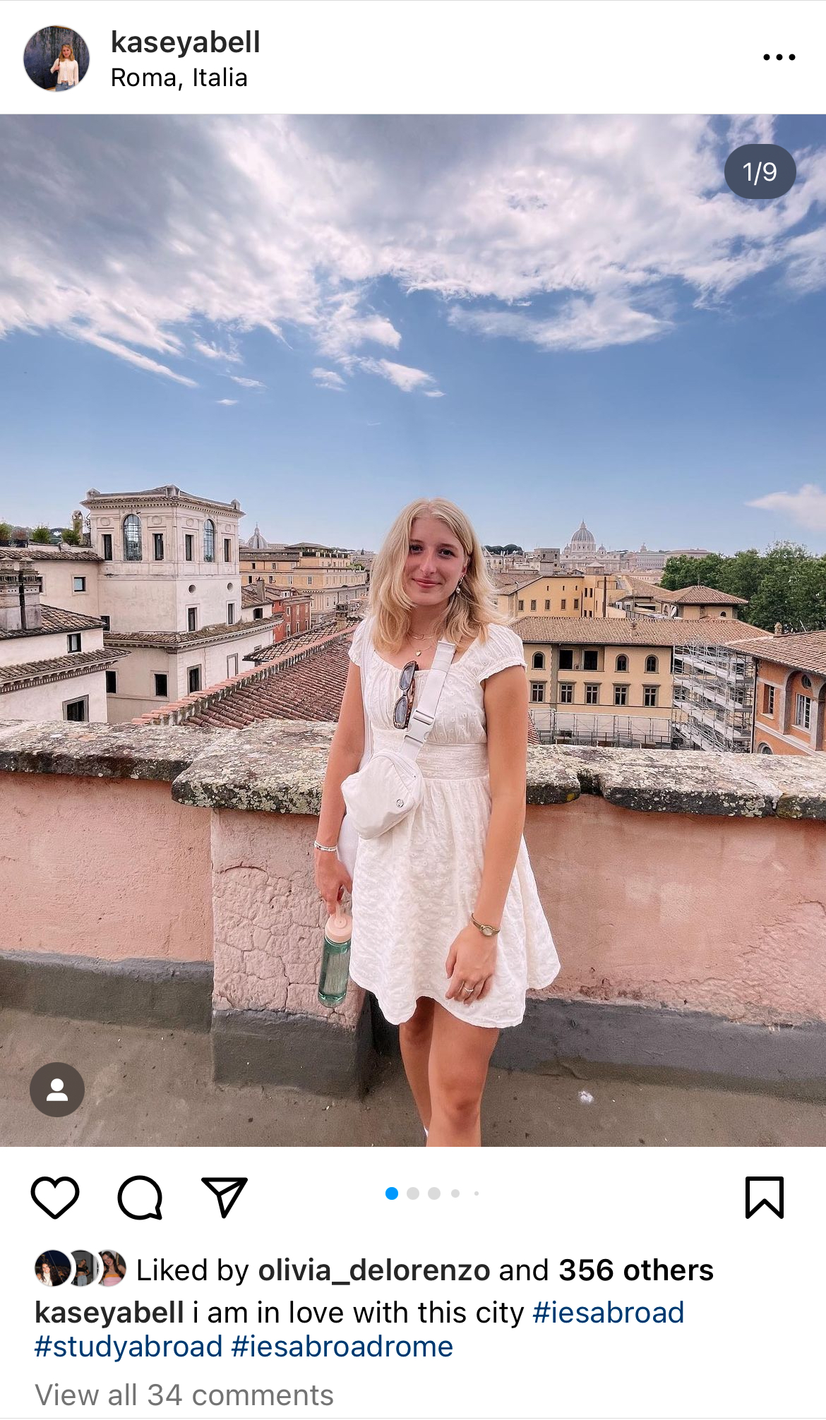 This instagram post depicts a young white blonde female wearing a cream short dress standing on a balcony with the rooftops of Rome behind her, and St.Peters Basillica in the distance.